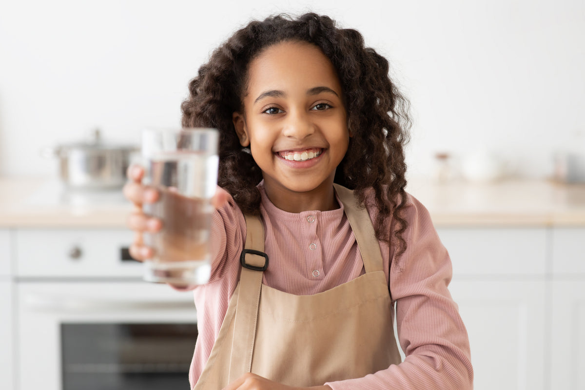 Smiling girl in a kitchen holding up a glass of water