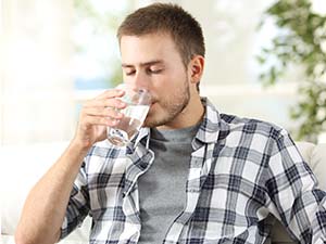 A young man drinking from a glass of water. 