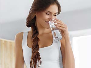  A smiling woman holding a glass of water standing at a kitchen counter.