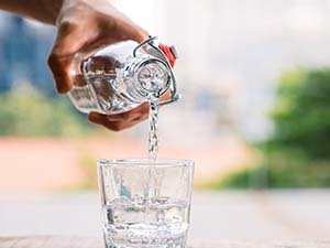 A man pouring water from a glass pitcher into a glass.