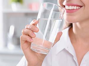A woman smiling as she brings a glass of water to her lips.