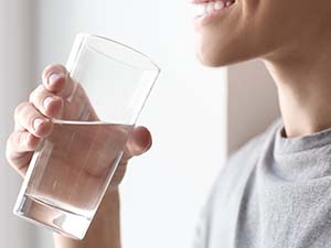 A smiling young man drinking a glass of water. 