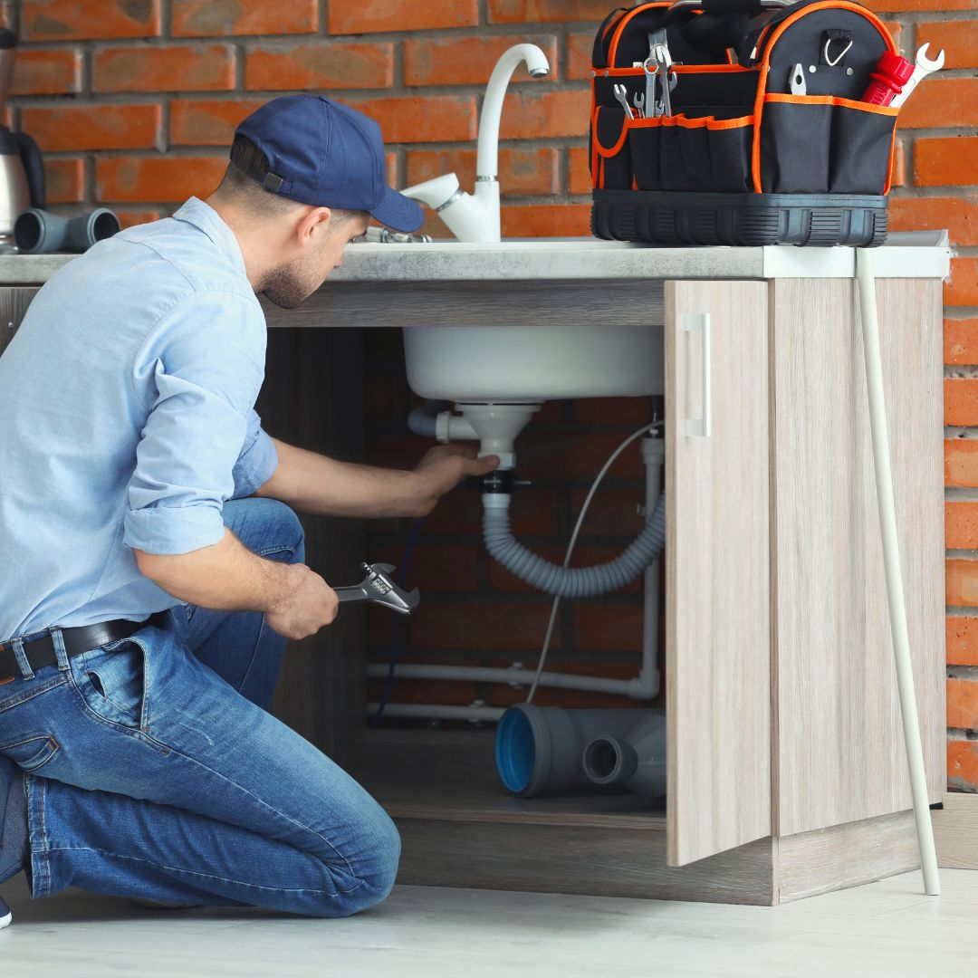 plumber working on drain under sink