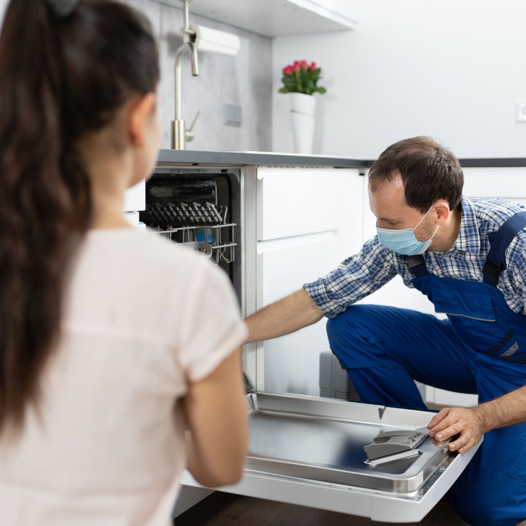 plumber repairing dishwasher while client watches