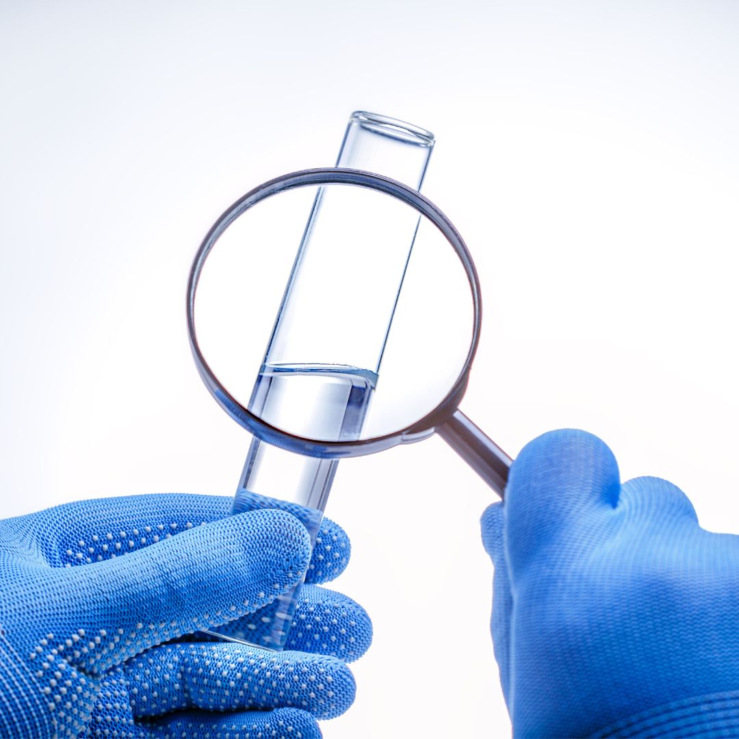 gloved hands examining tube of water with magnifying glass