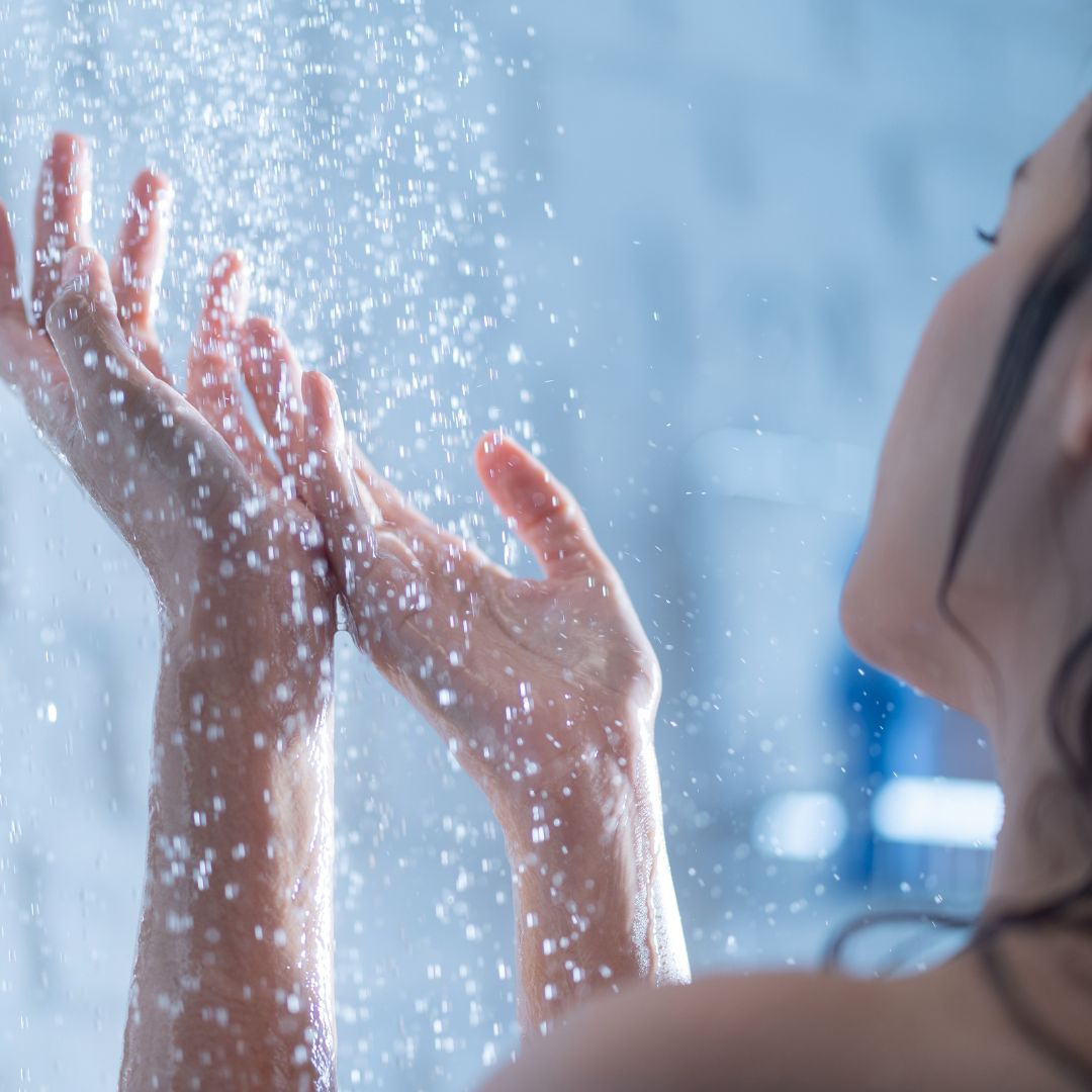 person holding out their hands into the water flowing from a shower head