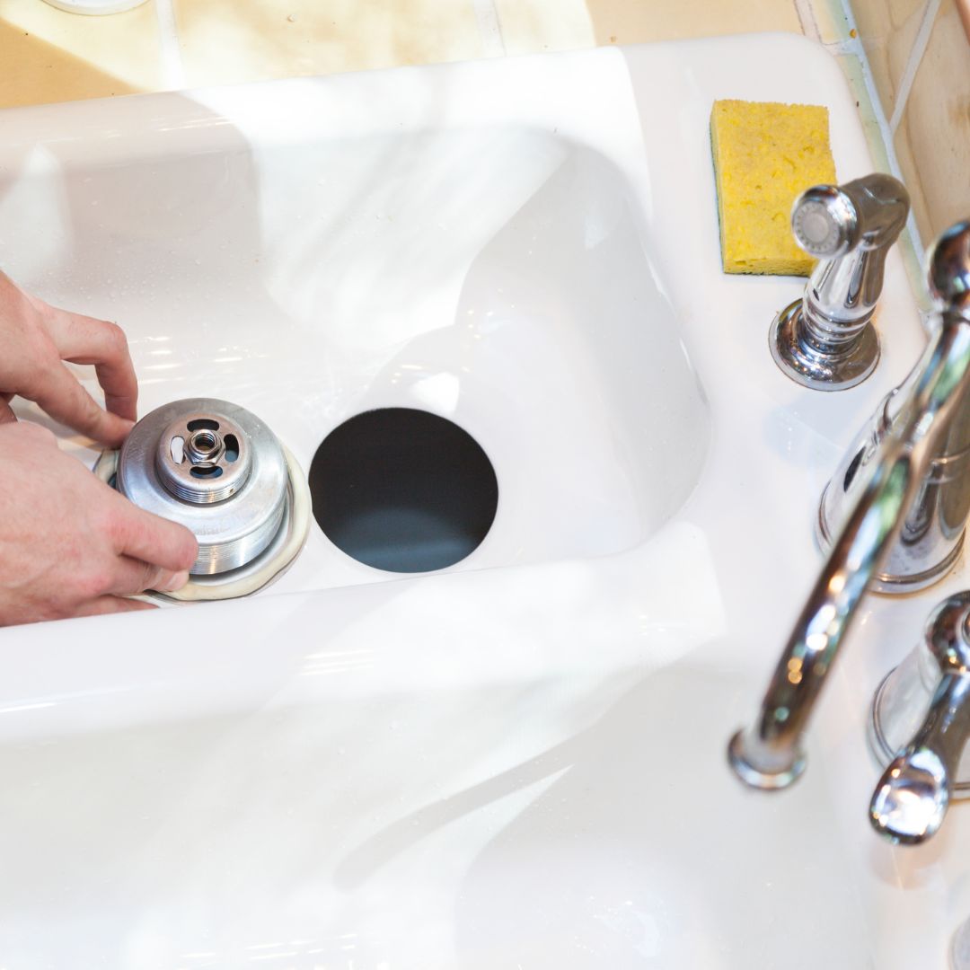 person removing drain fixture from kitchen sink