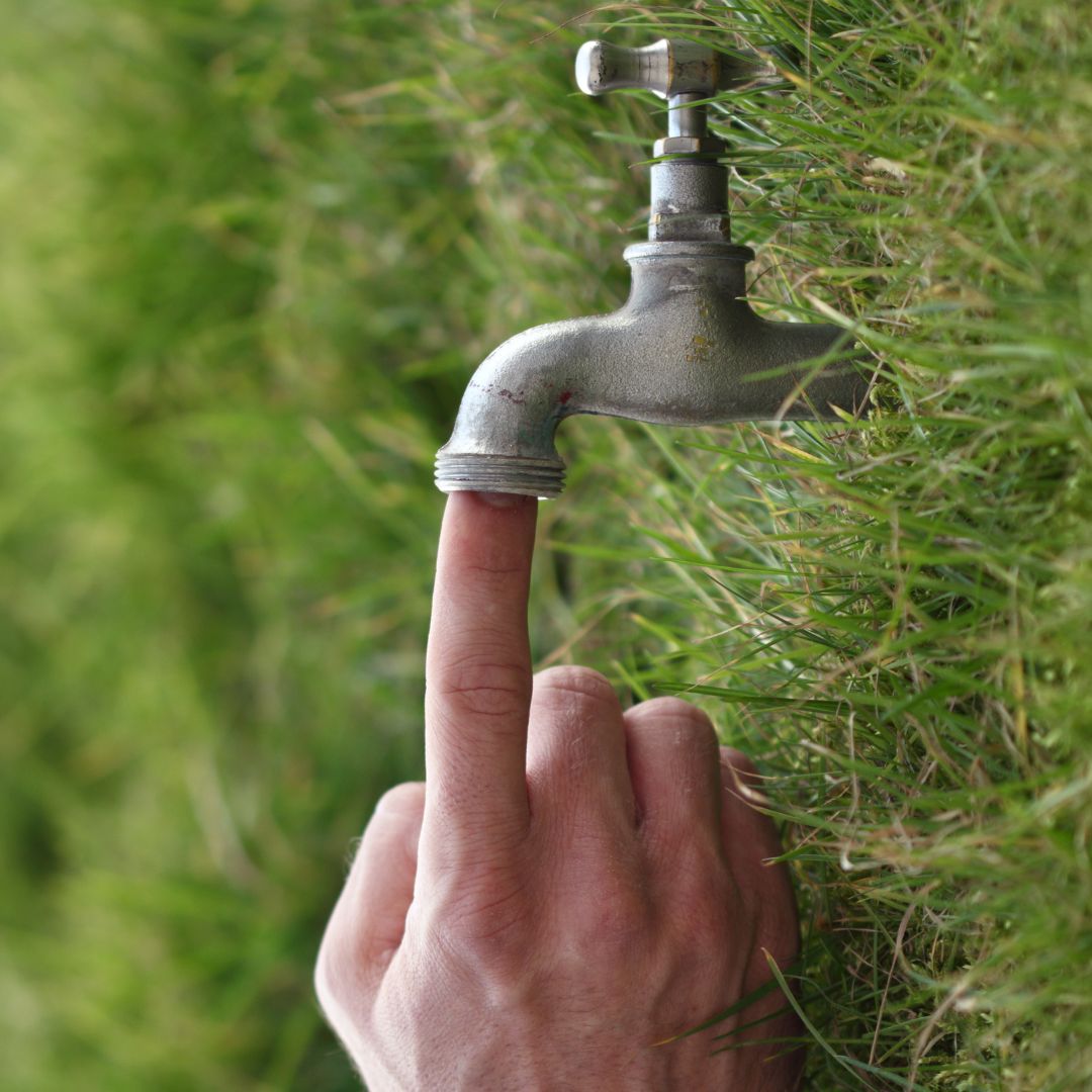 person plugging outdoor faucet with finger
