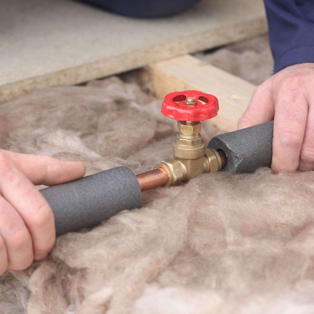 A person installing foam insulation around plumbing pipes