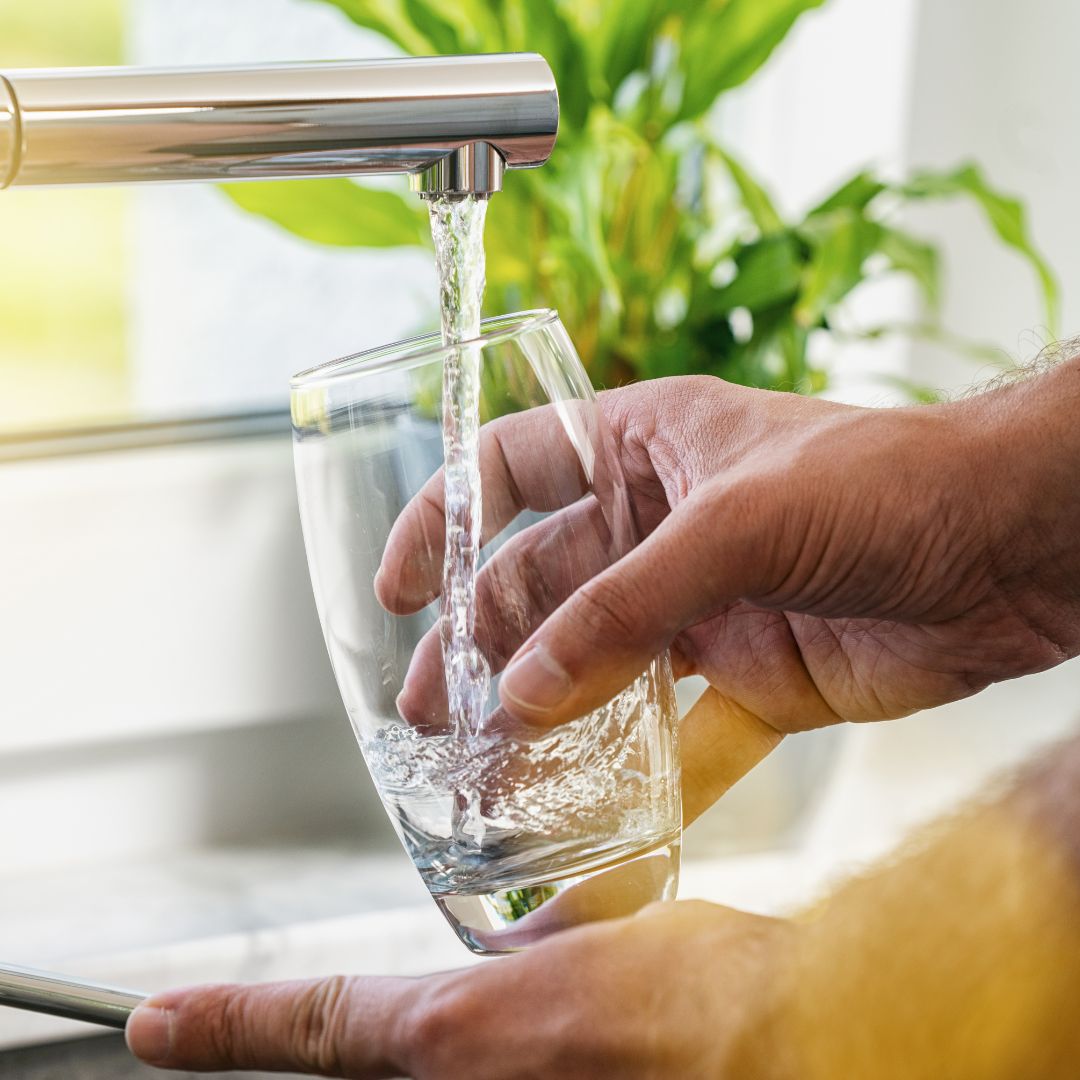 person pouring water into glass from faucet