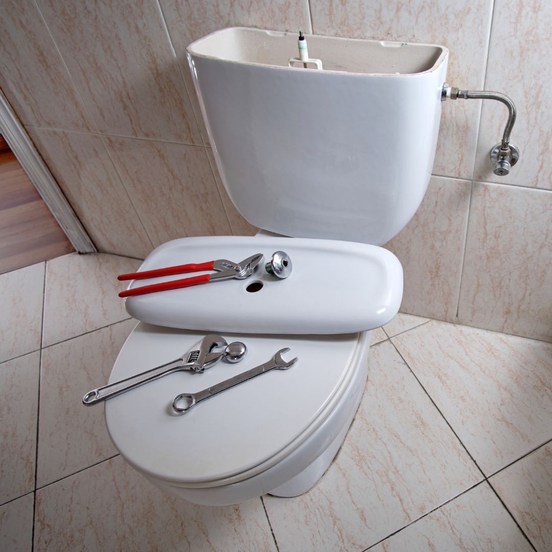 toilet with open tank and wrenches on seat