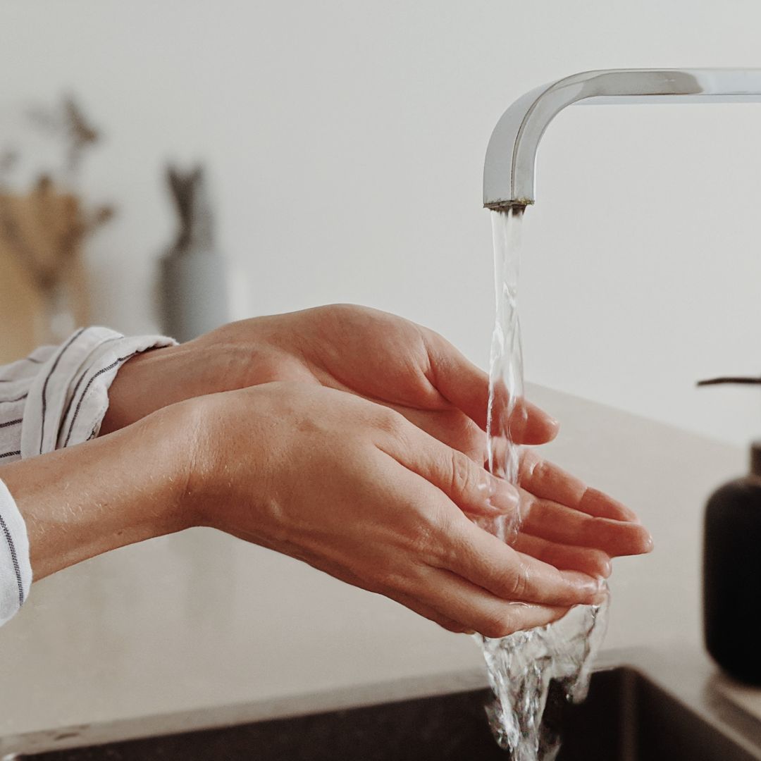 person holding hands under running water from a kitchen faucet